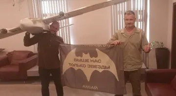Боєць несе Ось-25 на плечі, поруч прапор розвідбату «Аксай»